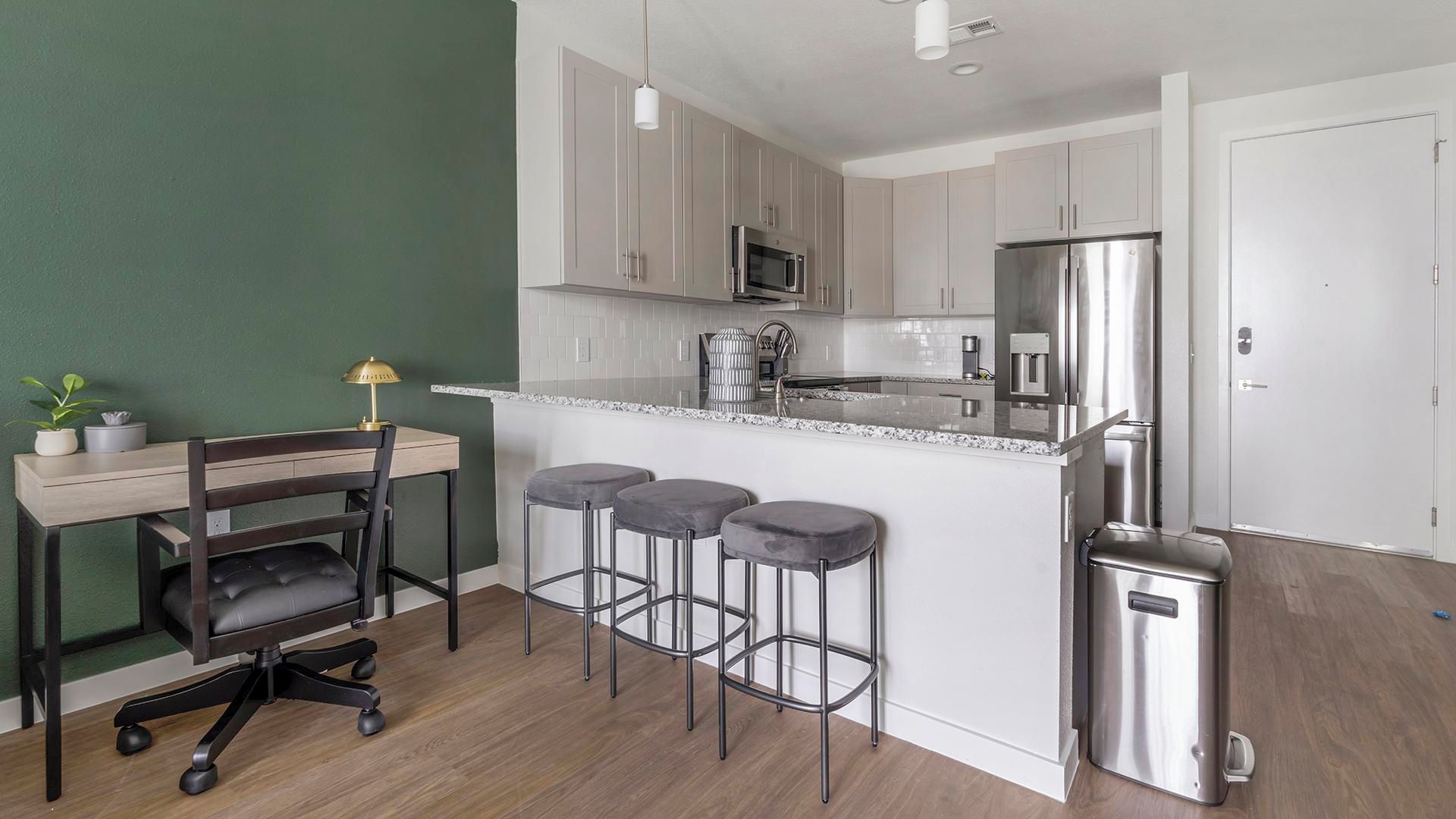 Une cuisine moderne dotée d’un îlot central, d’appareils électroménagers en acier inoxydable et d’un coin repas avec une chaise et des tabourets.
