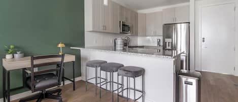 Une cuisine moderne dotée d’un îlot central, d’appareils électroménagers en acier inoxydable et d’un coin repas avec une chaise et des tabourets.