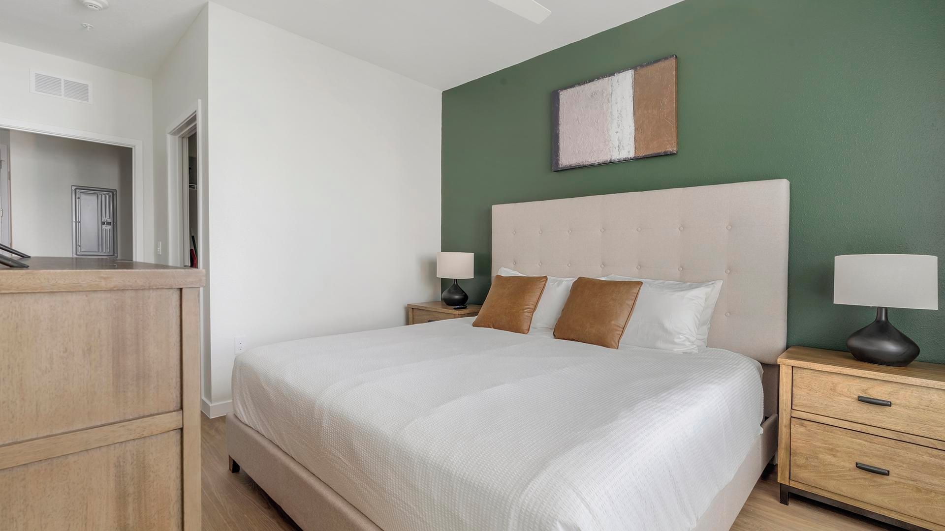 Quarto com cama, mesas de cabeceira, cômoda e parede verde.
