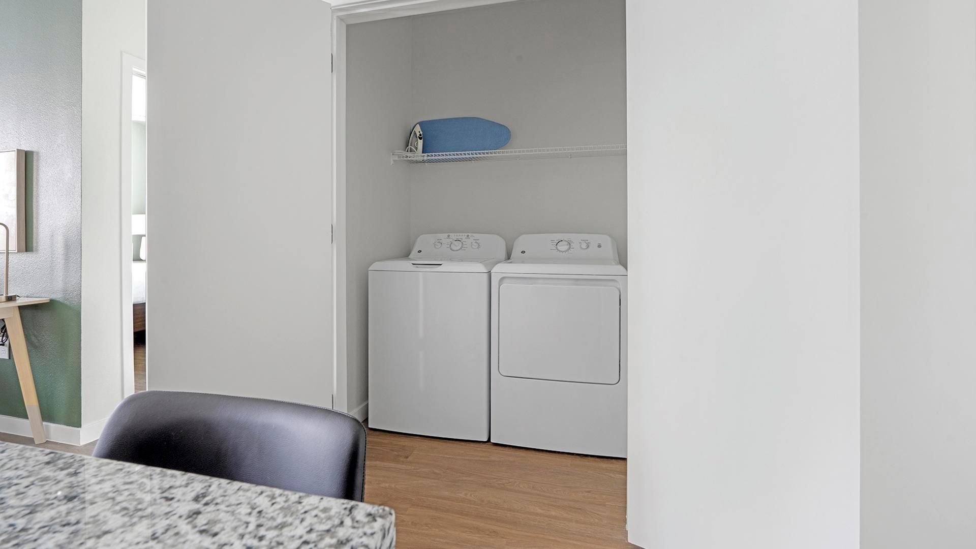 A laundry room with two white washing machines and a blue storage bin on a shelf.