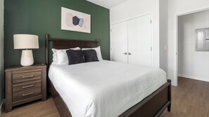 A bedroom with a bed, nightstand, dresser, and a door. - Landing | Spectacular 2BD, Yoga Studio, Gym (Sarasota)