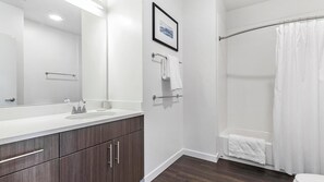 A bathroom with a white sink, dark wood cabinets, a large mirror, a framed picture, a towel rack, and a shower curtain. - Landing | Incredible 1BD, Yoga Studio, Gym (Sarasota)
