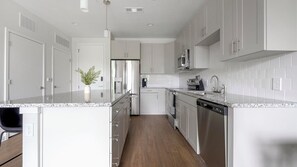 A modern kitchen with white cabinetry, stainless steel appliances, and a granite countertop. - Landing | Chic 1BD, Yoga Studio, Gym (Sarasota)