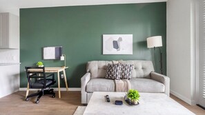 A living room with a green wall, a grey sofa, a wooden desk, a black office chair, a white coffee table, and a floor lamp. - Landing | Chic 1BD, Yoga Studio, Gym (Sarasota)