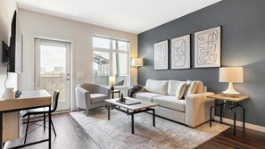 A modern living room with a sofa, armchairs, a coffee table, and a TV. - Landing | Incredible 1BD, Yoga Studio, Gym (Sarasota)