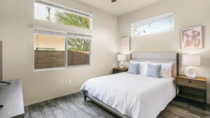 A bedroom with a bed, two bedside tables, a window, and artwork on the walls. - Landing | Spectacular 2BD, Gym, Yoga Studio (Sarasota)