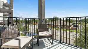 Ein Balkon mit Blick auf eine Straße und Gebäude, ein Tisch mit Stühlen und ein Geländer.