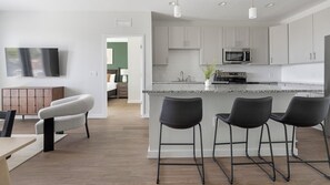A modern kitchen with a central island, bar stools, and a flat-screen TV mounted on the wall. - Landing | Modern 2BD, Gym, Yoga Studio (Sarasota)