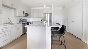 Eine moderne Küche mit weißen Schränken, Edelstahlgeräten, einer Granit Arbeitsplatte und schwarzen Barhocker.