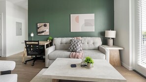 A modern living room with a grey sofa, a coffee table, a lamp, and a painting on the wall. - Landing | Modern 2BD, Gym, Yoga Studio (Sarasota)