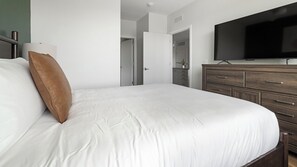 A bedroom with a bed, a dresser, a television, and a door leading to another room. - Landing | Modern 2BD, Gym, Yoga Studio (Sarasota)