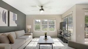 A living room with a sofa, a coffee table, a TV on a stand, a ceiling fan, and a window with blinds. - Landing | Incredible 2BD, Yoga Studio, Gym (Sarasota)