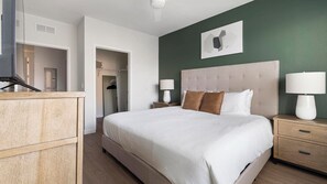 Una habitación de hotel con una cama grande, una mesita de noche con lámpara, un armario y un cuadro en la pared.