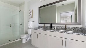 Un baño moderno con cabina de ducha de vidrio, inodoro, lavabo con un espejo grande y un perchero para toallas.