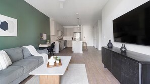 Una sala de estar moderna con un sofá gris, una mesa de centro blanca y una cocina al fondo.