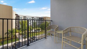 A balcony with two wicker chairs, a view of a residential area, and a clear sky. - Landing | Beautiful 1BD, Gym, Yoga Studio (Sarasota)