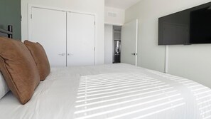 Een slaapkamer met een bed, een aan de muur bevestigde televisie en een kledingkast.