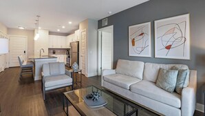 Una sala de estar moderna con un sofá, una mesa de centro de vidrio y una cocina al fondo.