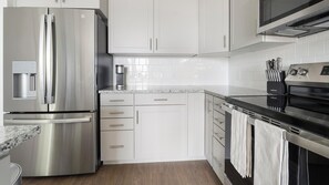 Een moderne keuken met roestvrijstalen apparatuur, witte kasten en een granieten aanrecht.