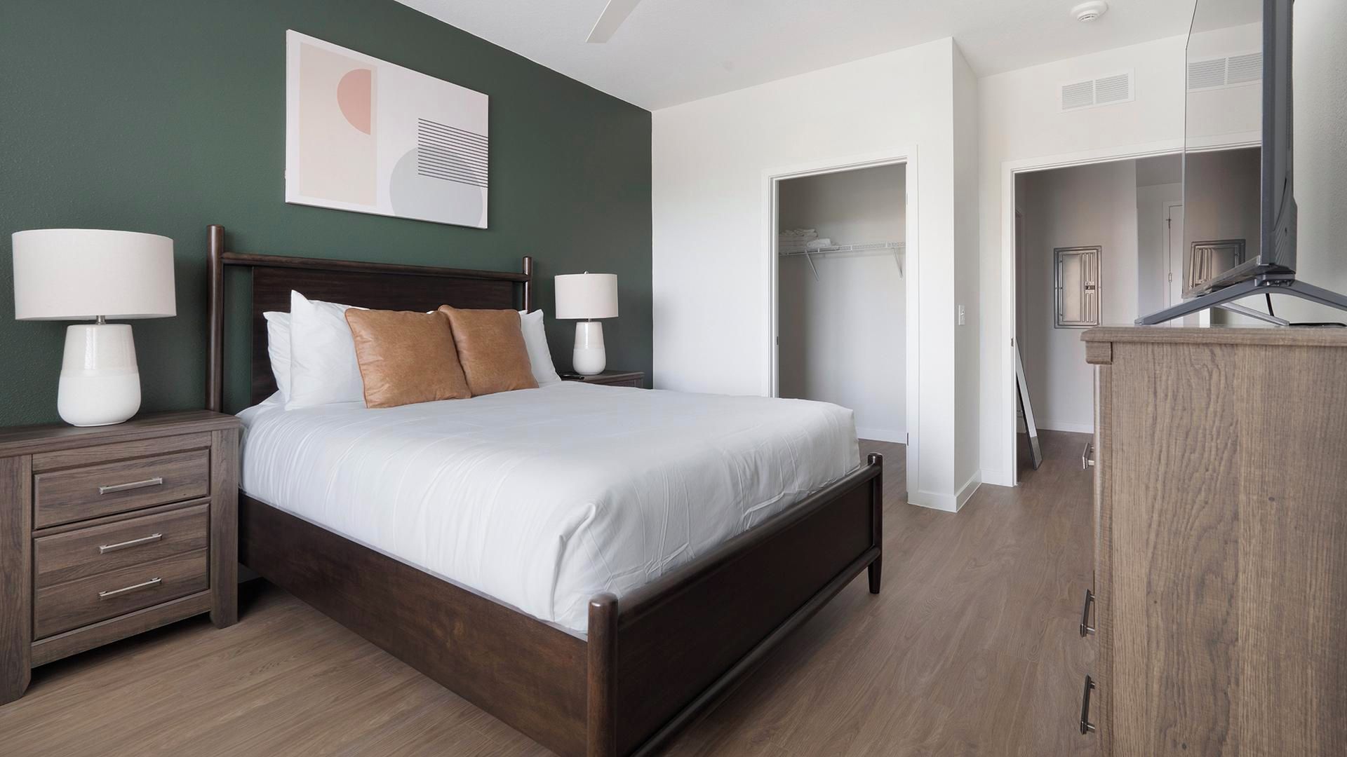 A bedroom with a bed, nightstands, a dresser, and a walk-in closet.