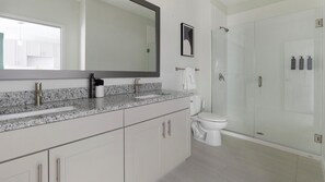 Een moderne badkamer met een granieten blad, toilet, douchecabine en een grote spiegel.