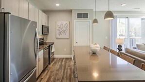 Une cuisine moderne dotée d’appareils électroménagers en acier inoxydable, d’un plancher en bois, d’un îlot central, de luminaires suspendus et offrant une vue sur l’extérieur.