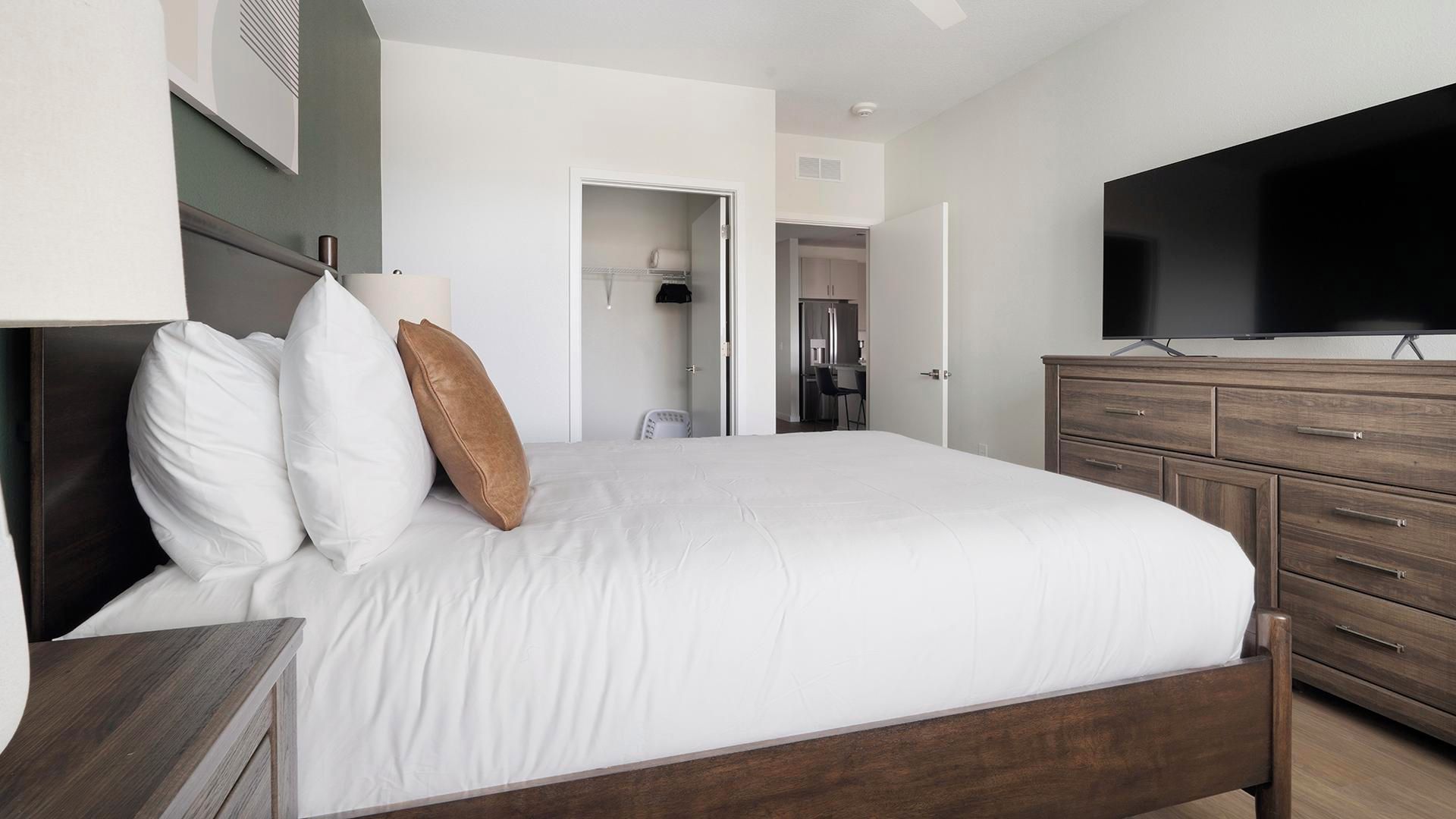 A hotel room with a bed, a TV, a dresser, and a bathroom visible through an open door.