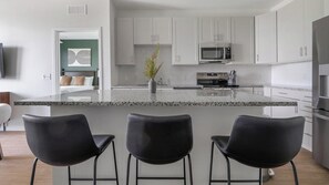 A modern kitchen with white cabinets, a granite countertop, a built-in microwave, and a stainless steel refrigerator. - Landing | Amazing 2BD, Gym, Yoga Studio (Sarasota)