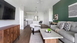 A modern living room with a sofa, coffee table, and a TV mounted on the wall. - Landing | Amazing 2BD, Gym, Yoga Studio (Sarasota)