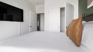 Habitación de hotel con una cama, un televisor montado en la pared y un armario con la puerta abierta.