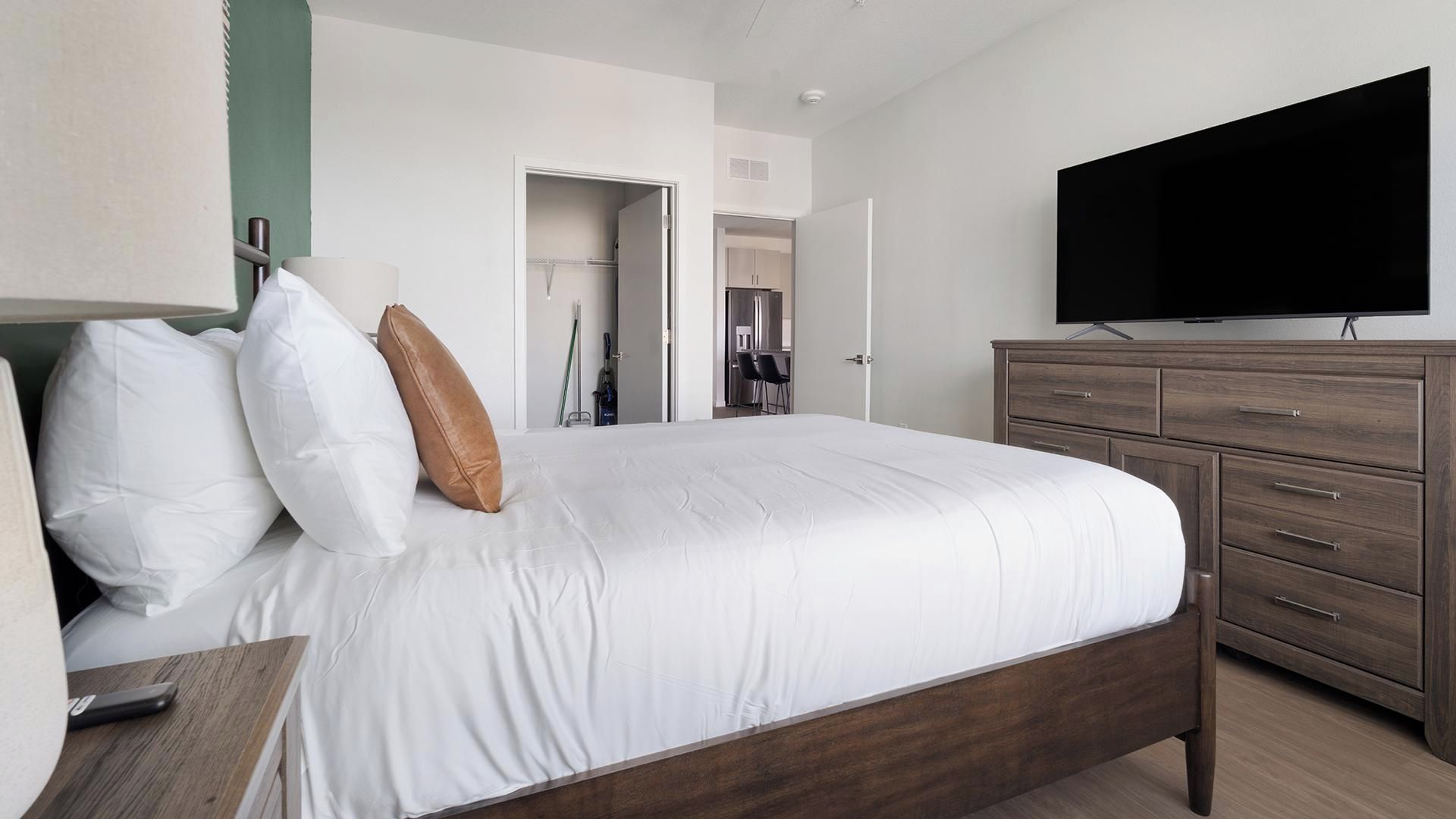 A hotel room with a bed, a television, a dresser, and a door leading to a bathroom.