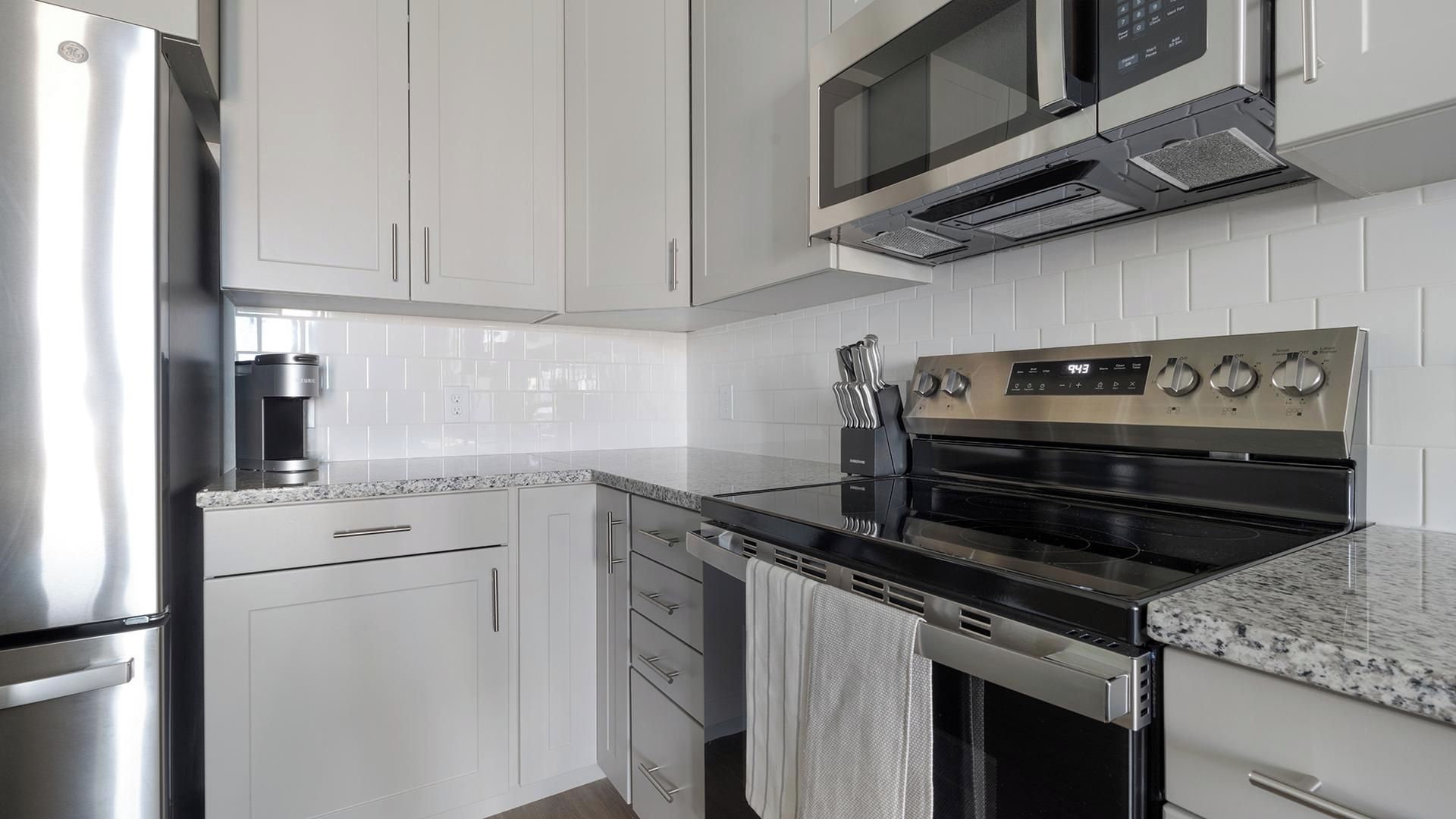 A modern kitchen with stainless steel appliances, white cabinetry, and a granite countertop.