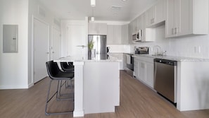 A modern kitchen with white cabinetry, stainless steel appliances, and a central island with bar stools. - Landing | Spectacular 1BD, Gym, Yoga Studio (Sarasota)