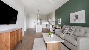 Ein modernes Wohnzimmer mit einem grauen Sofa, einem Holztisch und einem an der Wand befestigten Fernseher.