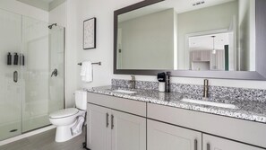 Et stilfuldt badeværelse med brusekabine i glas, toilet, stort spejl og bordplader i granit.