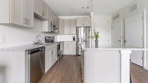 A modern kitchen with stainless steel appliances, white cabinetry, and a granite countertop. - Landing | Beautiful 1BD, Yoga Studio, Gym (Sarasota)