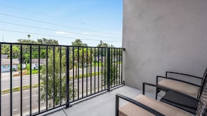 A balcony with a metal railing, a concrete floor, and a view of a street with houses and trees. - Landing | Beautiful 1BD, Yoga Studio, Gym (Sarasota)