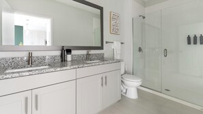A modern bathroom with a granite countertop, a white toilet, a glass shower enclosure, and a large mirror. - Landing | Stylish 1BD, Gym, Yoga Studio (Sarasota)