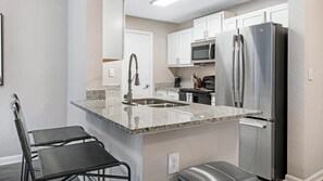 A modern kitchen with granite countertops, stainless steel appliances, and white cabinetry. - Landing | Stunning 1BD, Yoga Studio, Gym (Sarasota)