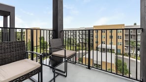 Ein Balkon mit zwei Korbstühlen und einem Tisch, mit Blick auf ein Wohngebiet mit Gebäuden und Grünflächen.
