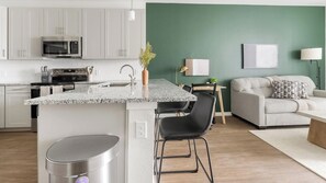 A modern kitchen with a granite countertop, stainless steel appliances, and a dining area with a table and chairs. - Landing | Stylish 1BD, Gym, Yoga Studio (Sarasota)