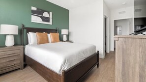 A hotel room with a bed, nightstands, a desk, and a painting on the wall. - Landing | Stylish 1BD, Gym, Yoga Studio (Sarasota)