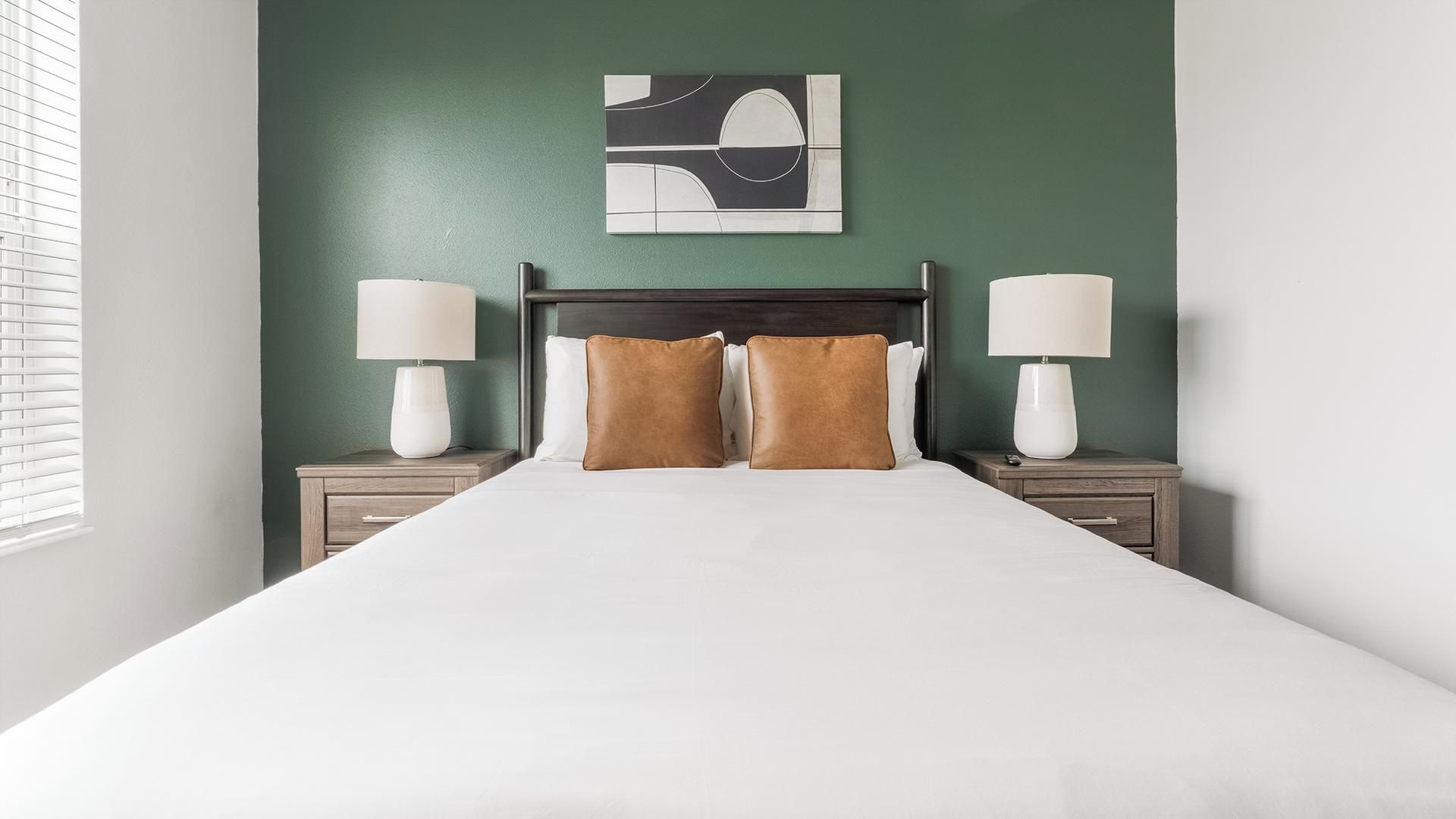 A hotel room with a bed, two bedside tables with lamps, a headboard, and a wall art piece.