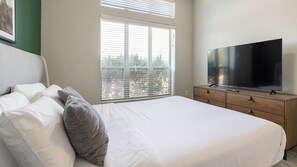 Ein Schlafzimmer mit einem Bett, einem Fernseher auf einer Holzkommode und einem Fenster mit Jalousien.