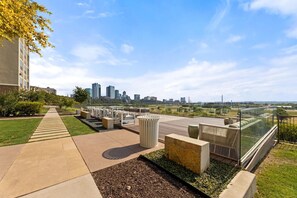 A rooftop terrace with outdoor seating, a pathway leading to a building, and a city skyline in the background. - Landing | Incredible 2BD, Rooftop Lounge (Fort Worth)