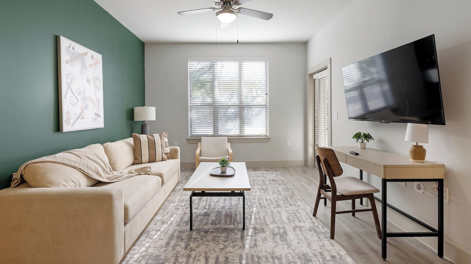 A living room with a sofa, a coffee table, a TV, and a desk with a chair.