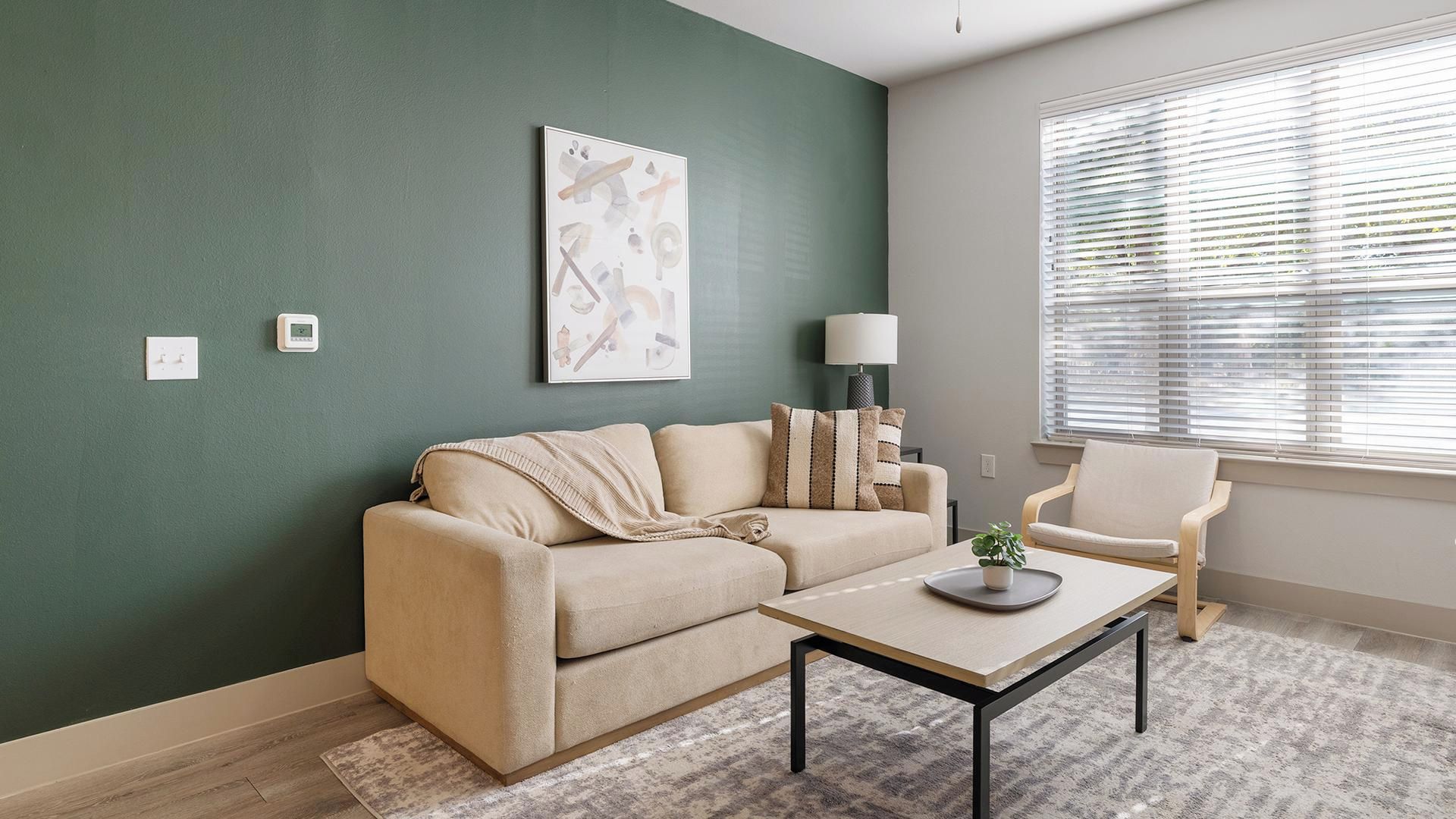 A living room with a beige sofa, a coffee table, a lamp, and a window with blinds.