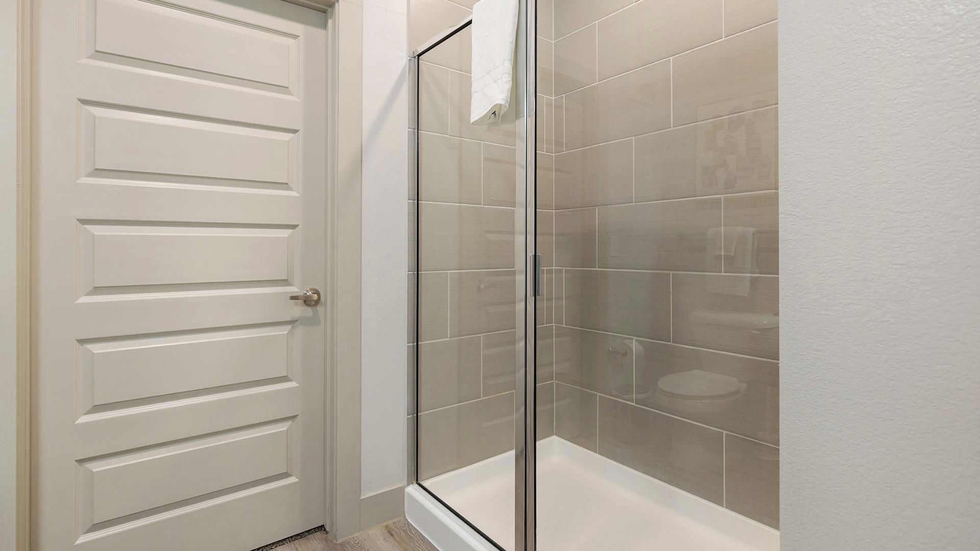 A bathroom with a glass shower enclosure, a white door, and tiled walls.
