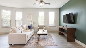 Ein Wohnzimmer mit einer Couch, einem Couchtisch, einem Sessel, einem Fernseher und einem Deckenventilator.