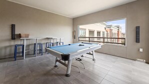 Une table de billard dans une pièce donnant sur des bâtiments, avec vue par le biais d’un balcon.